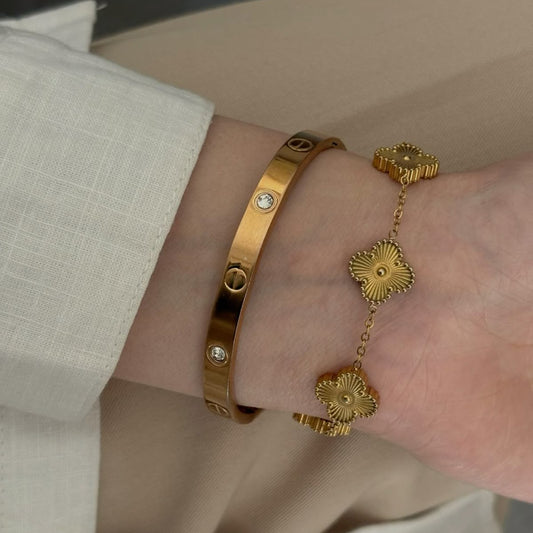Luxury jewelry set including Cartier cuff and golden clover bangle, adjustable fit.