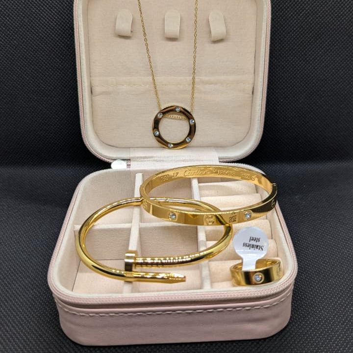 A 4-piece set of gold-toned jewelry made of Stainless Steel, including a circle pendant necklace, two iconic-style bangles (one with clear stones and one in a nail/clou design), and a stone-accented ring. The set is displayed in an open pink travel jewelry box, emphasizing the waterproof and 70% off sale