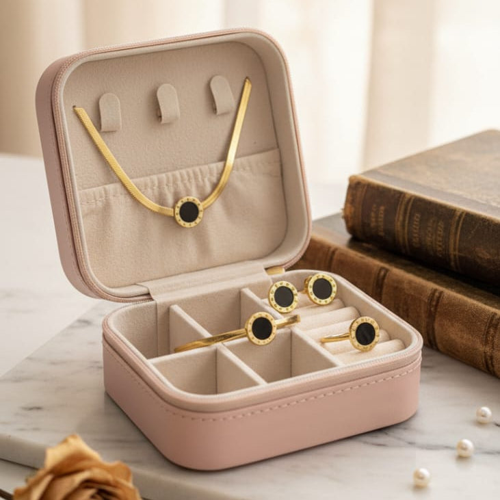A 4-piece jewelry set featuring black circular enamel and gold detailing (snake chain necklace, bracelet, ring, and stud earrings) beautifully displayed inside an open, blush pink travel jewelry box on a marble surface, emphasizing the waterproof and 70% off sale offer.