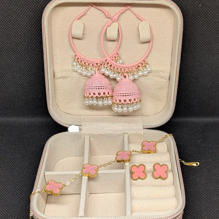 A curated 4-piece jewelry set in a pink travel box, featuring a gold-toned pink enamel four-petal (clover) bracelet and matching stud earrings, alongside a pair of large pink hoop earrings with traditional pearl-accented jhumka bells. The set is waterproof (clover items) and 70% off.