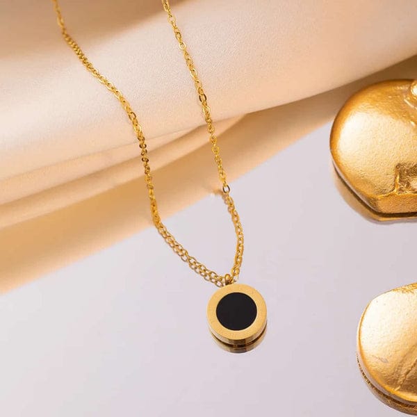 Elegant black and gold round pendant necklace on reflective surface