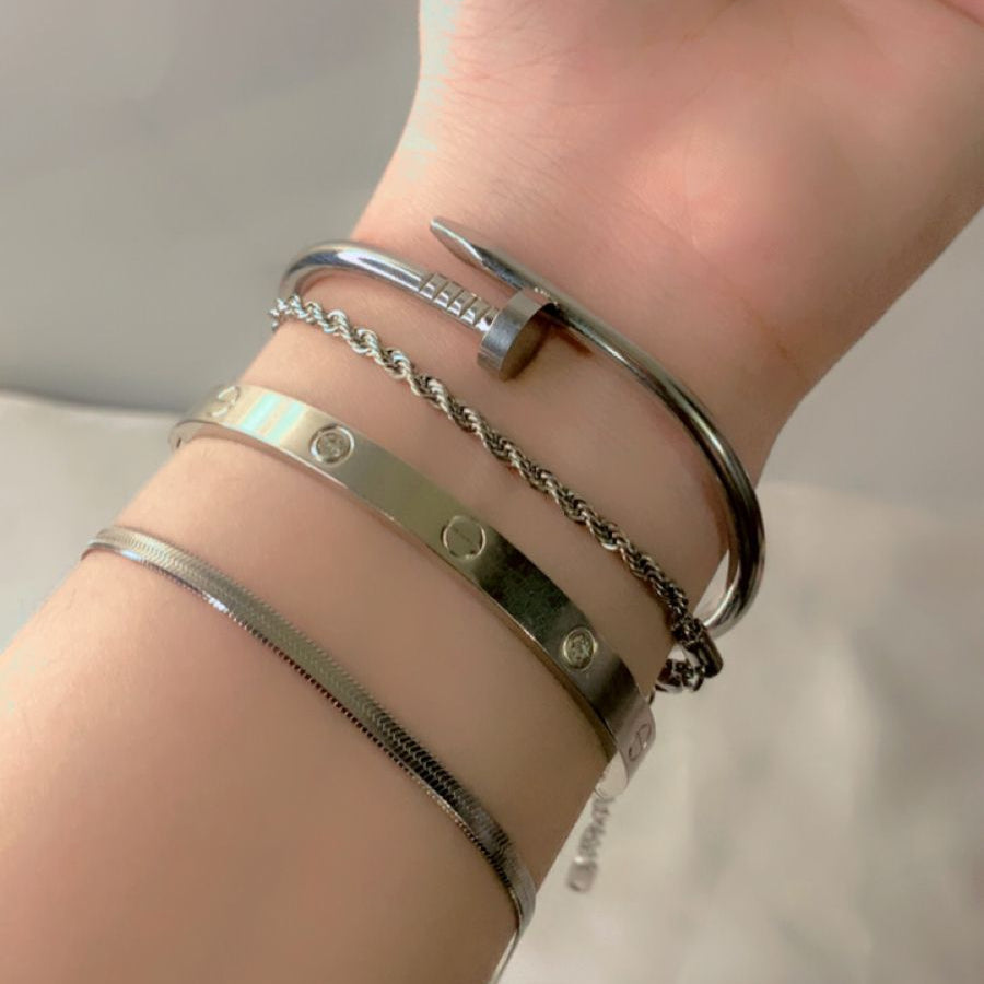 The bracelets include a polished silver bangle, a twisted chain design, and a minimalistic studded bracelet
