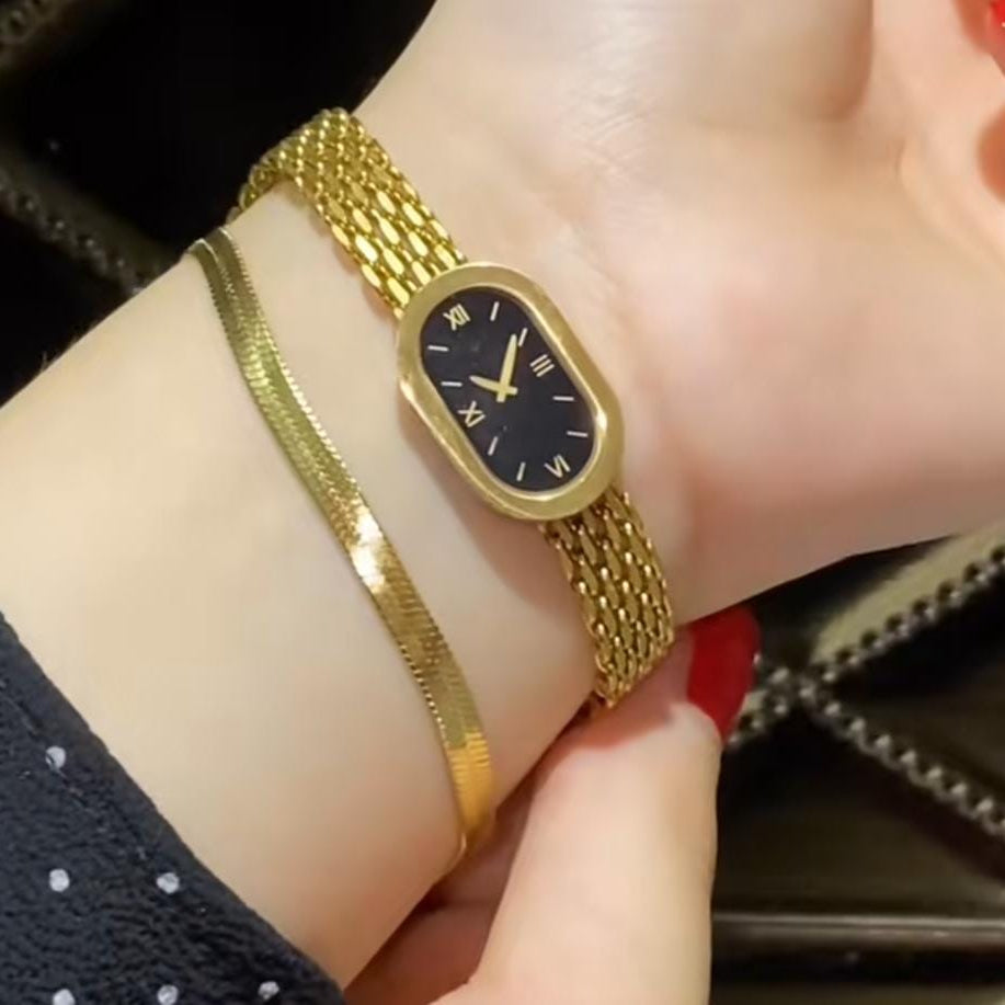 gold-plated mesh watch with a black dial, worn with a matching thin gold bracelet