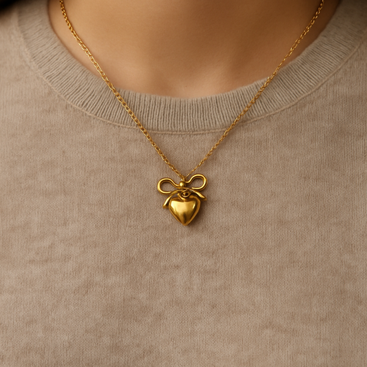 Delicate gold bow heart pendant necklace worn with casual top.