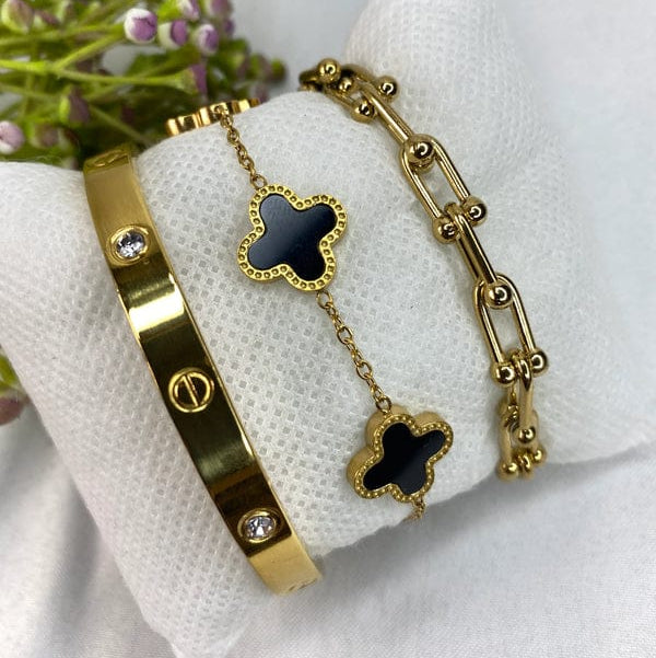 a solid bangle with screw motifs and crystals, a delicate chain bracelet with black clover charms, and a hardware U-link bracelet with beaded details.
