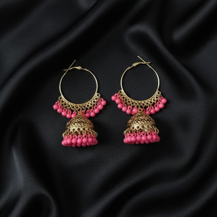 The earrings feature a round hoop from which the decorative bell-shaped Jhumka hangs. Both the hoop and the bell are adorned with a full, vibrant fringe of small, bright pink bead charms.