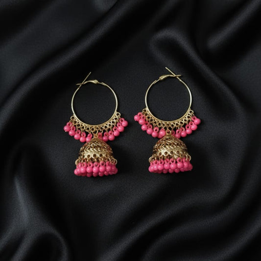 The earrings feature a round hoop from which the decorative bell-shaped Jhumka hangs. Both the hoop and the bell are adorned with a full, vibrant fringe of small, bright pink bead charms.