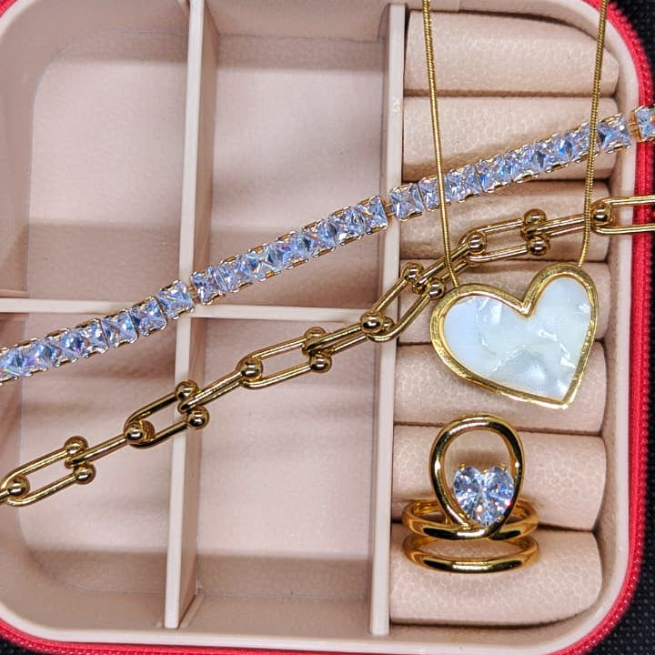 Gold jewelry set with heart-shaped pendant necklace, sparkling bracelet, and a matching heart-shaped ring, arranged in a red jewelry box.