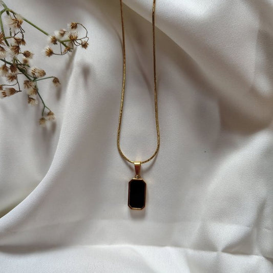 A gold snake chain necklace with a vertical black rectangular pendant