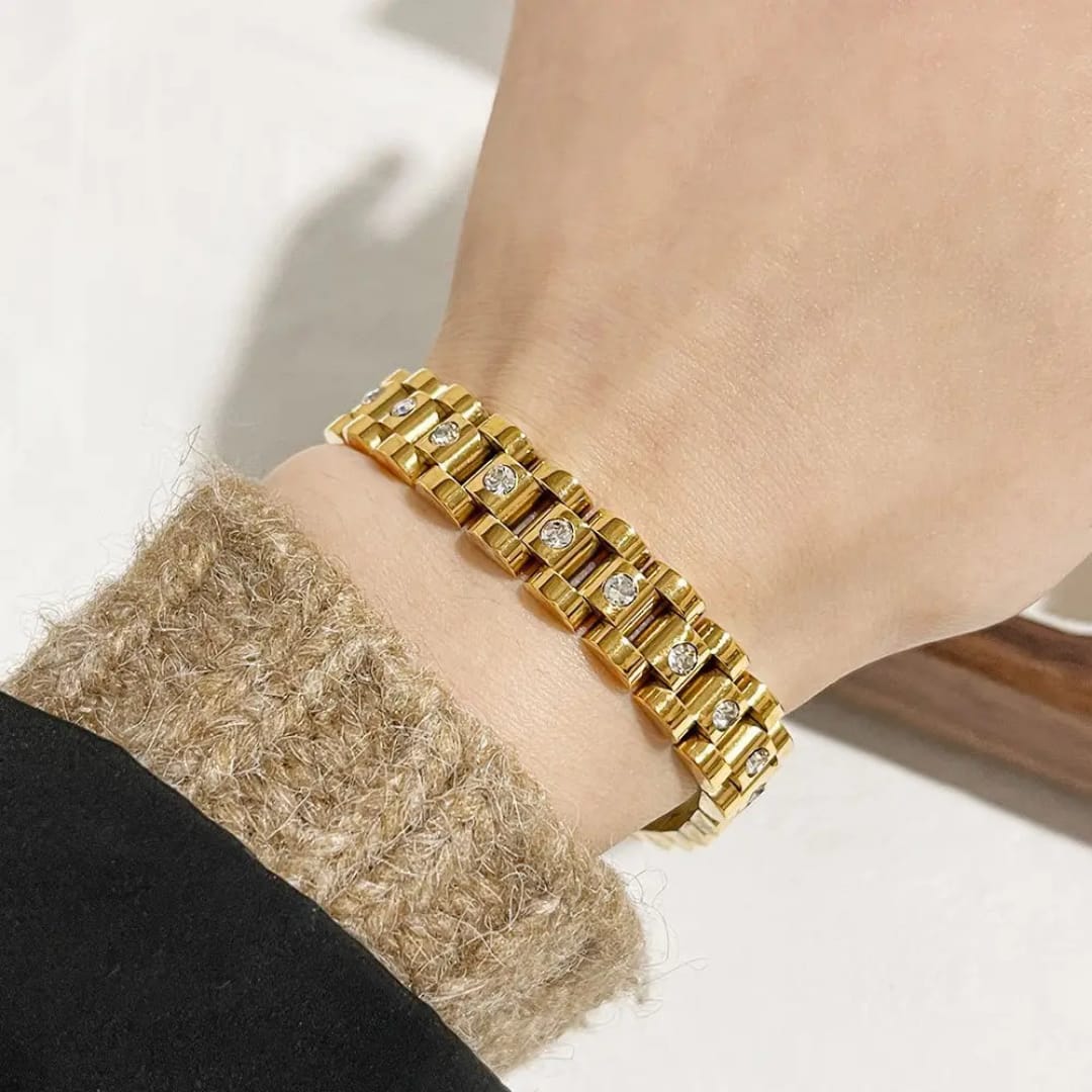 Gold Cuban link bracelet with crystal accents displayed in a wooden and white cushioned jewelry box on a light background.