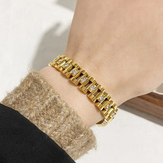 Gold Cuban link bracelet with crystal accents displayed in a wooden and white cushioned jewelry box on a light background.