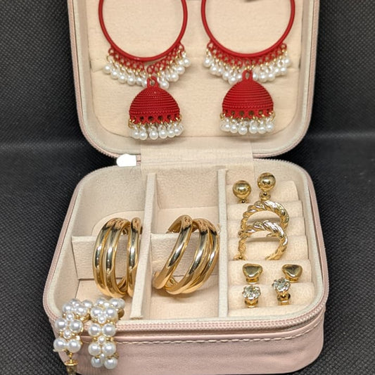 A large collection of earrings and rings displayed in a pink travel jewelry box. The set includes large red hoops with pearl-accented jhumka bells, chunky triple gold hoops/rings, and a variety of gold stud and dangle earrings. The gold items are waterproof, and the entire set is 70% off.