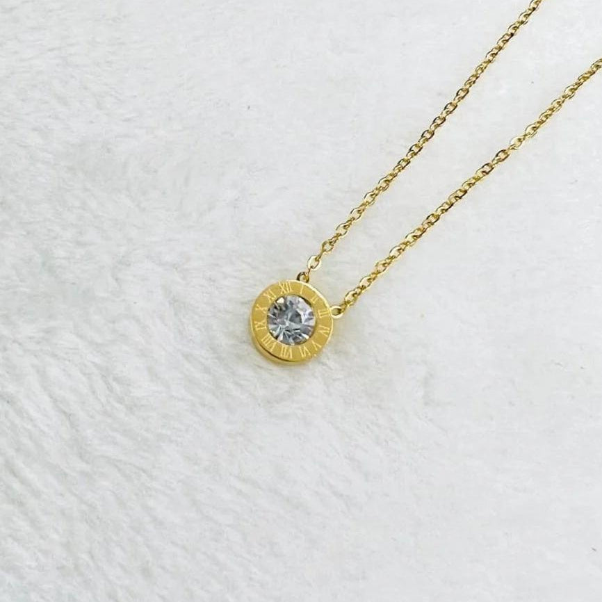 Gold pendant necklace with Roman numerals and a sparkling crystal center on a delicate gold chain