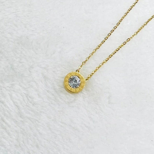 Gold pendant necklace with Roman numerals and a sparkling crystal center on a delicate gold chain