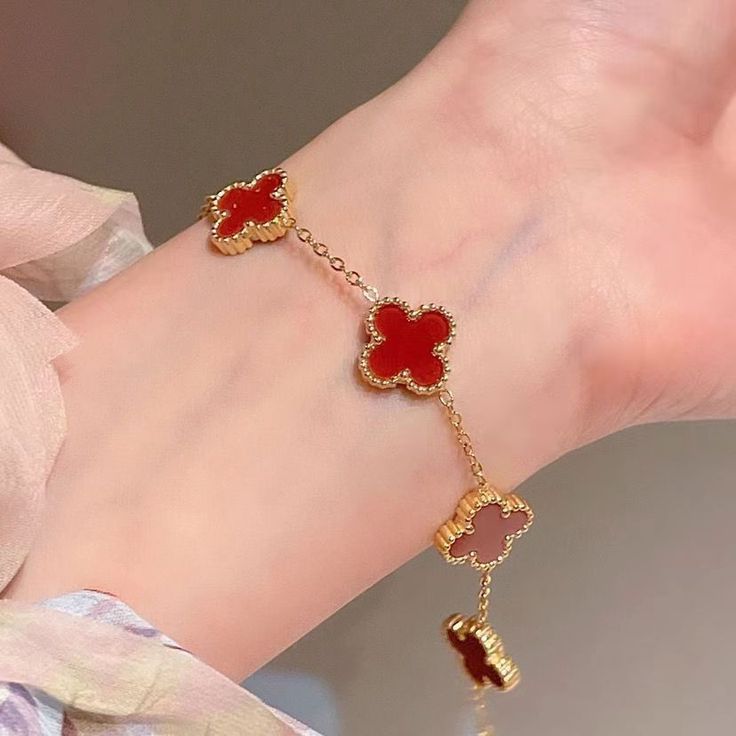Gold bracelet with five red clover charms placed on white satin fabric; waterproof, anti-tarnish, premium feminine jewelry piece.