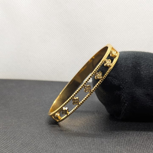 A polished gold-tone bangle bracelet with a black inlay and repeating gold clover motifs