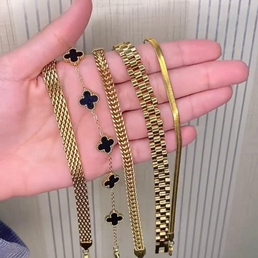 A hand holding five luxurious gold bracelets including mesh, chain, clover charm, square-link, and slim strip designs; premium waterproof and anti-tarnish jewelry set for women.