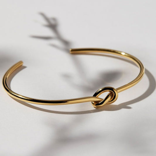 Minimalist gold knot bangle with a sleek polished finish, symbolizing elegance and connection, displayed on a clean white background.